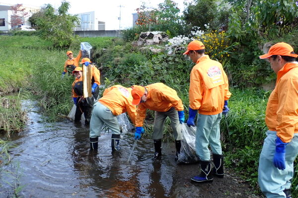 参加者の一部は胸まで覆う防水の胴長を着用しています。川の水中からゴミを拾っています。