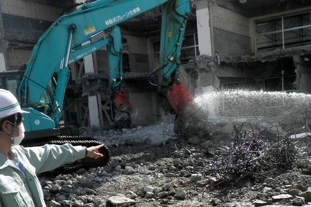 当財団職員が解体工事の立会いをしています。水をかけながら重機でコンクリートを破砕しています。