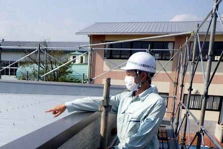 当財団職員が屋根の確認をしています。足場の上から屋根材を見ています。