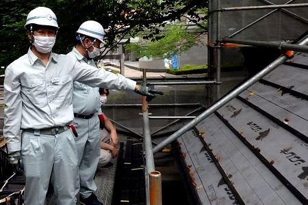 当財団職員が屋根下地の確認をしています。屋根足場やルーフィングシートが見えます。