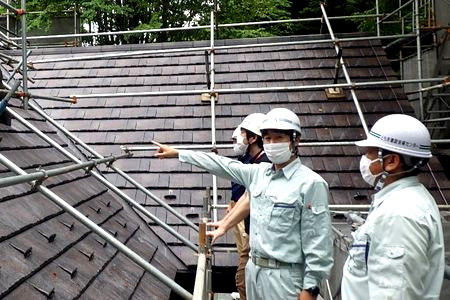 当財団職員が屋根の仕上がりを確認しています。屋根足場や屋根瓦が見えます。