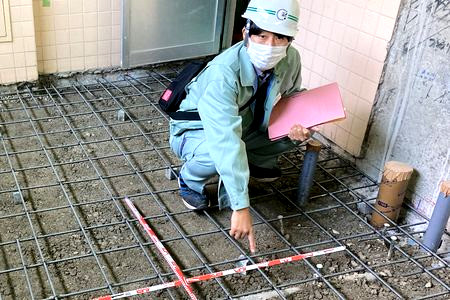 当財団職員が土間の配筋検査をしています。鉄筋やその間隔を測る赤白の標尺が見えます。