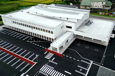 塩谷町新庁舎を上空から撮影しました。白い2階建ての建物本体と黒い駐車場が見えます。